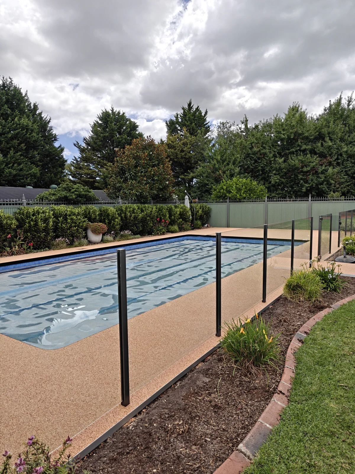 Completed resin-bound stone pool surround with glass fencing