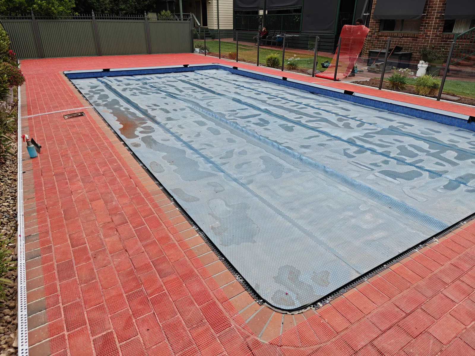 Dated red brick pool pavers with pool cover, taken from the house side looking down