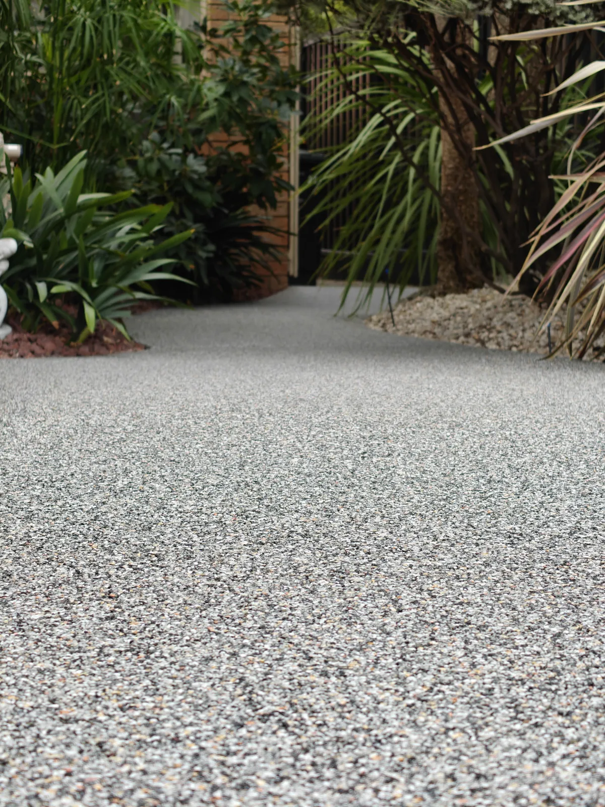 Low angle of grey stone garden path showing natural aggregate texture, gate and plants in background