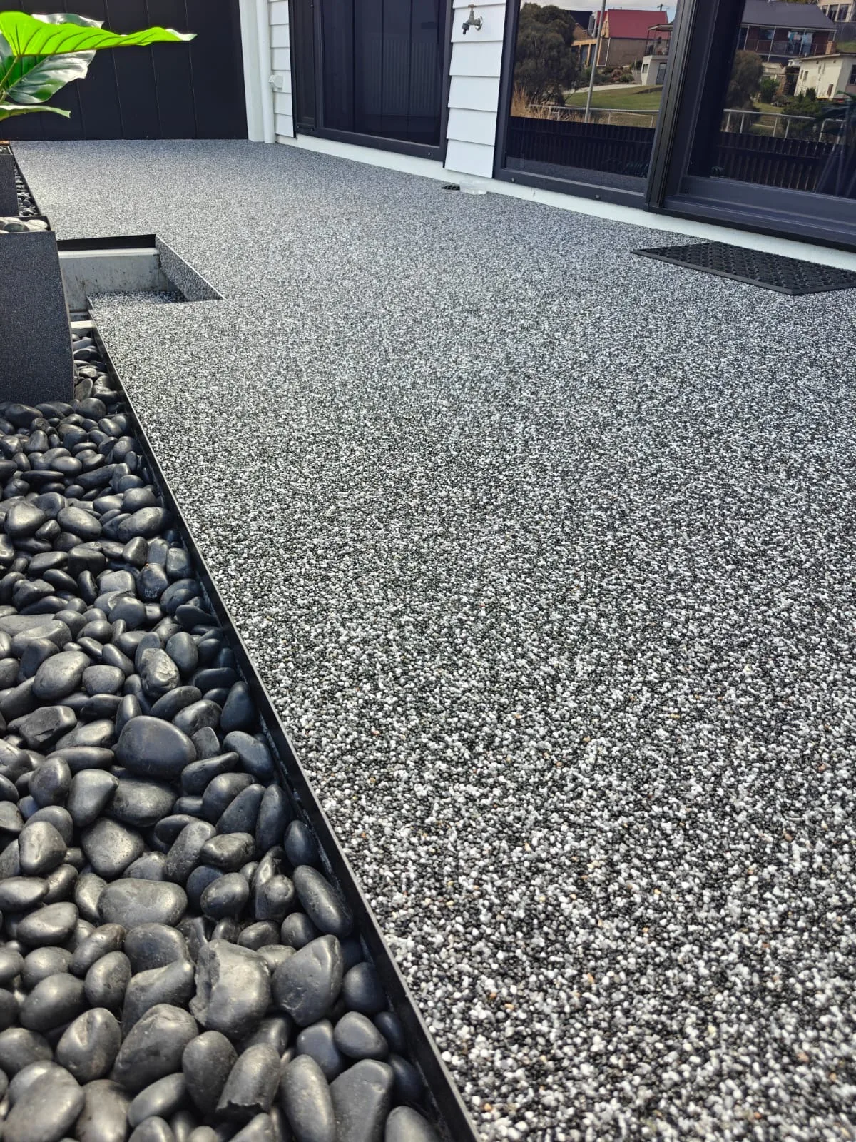 Dark resin-bound stone entry beside black river pebbles and charcoal trim