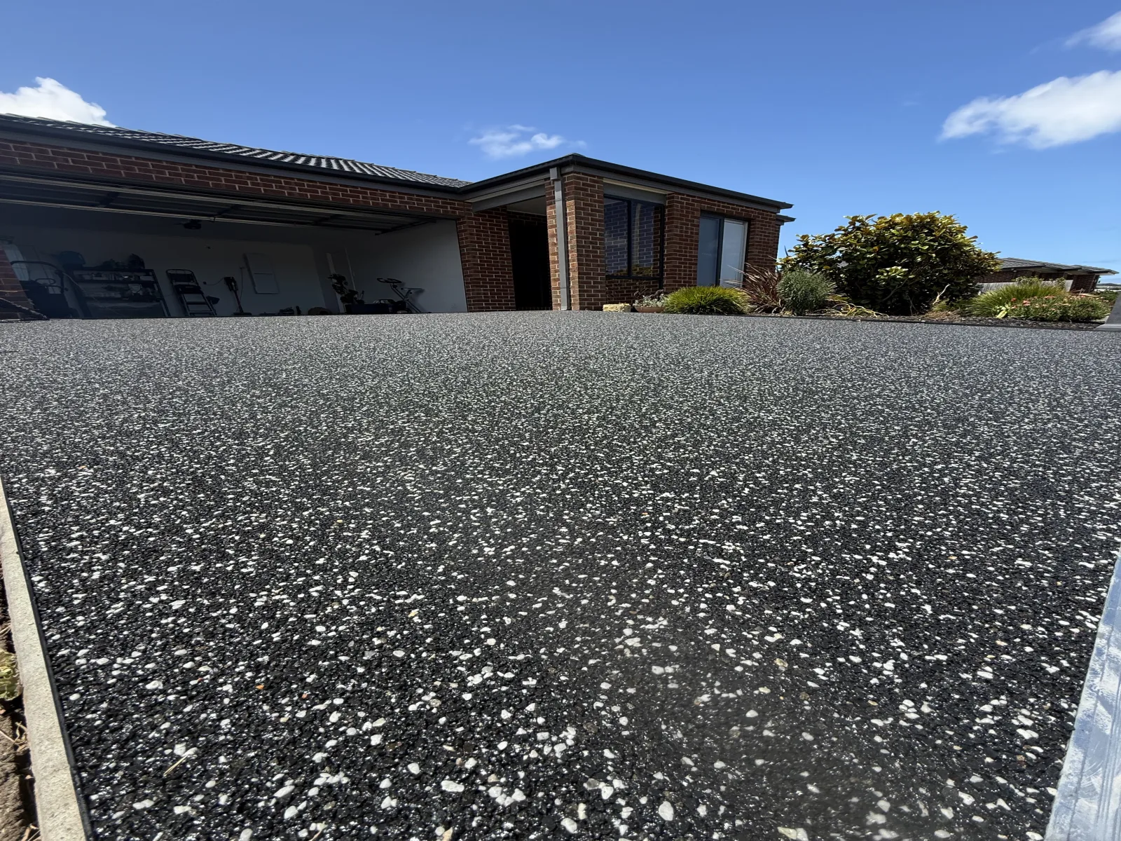 Black resin-bound stone driveway at a brick home under a clear blue sky