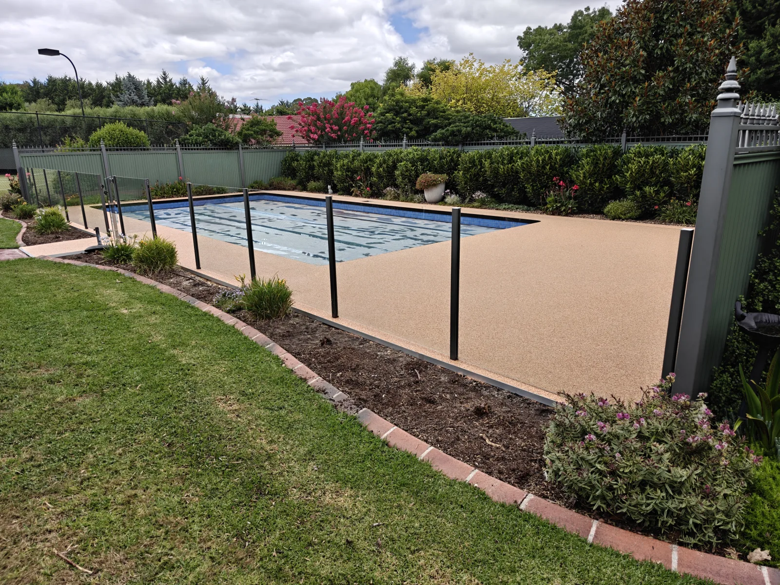 Warm stone pool surround with glass fencing and garden beds